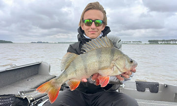 A happy angler proudly shows off a large perch she caught from her fishing boat