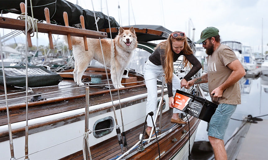 A couple with their dog on the deck of a boat at a marina, with the man holding the battery to show its marine application