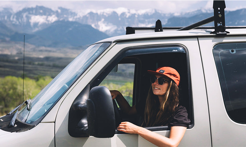 A woman in the driver's seat of a camper van in a mountainous region, showing the battery's use for RV and van life