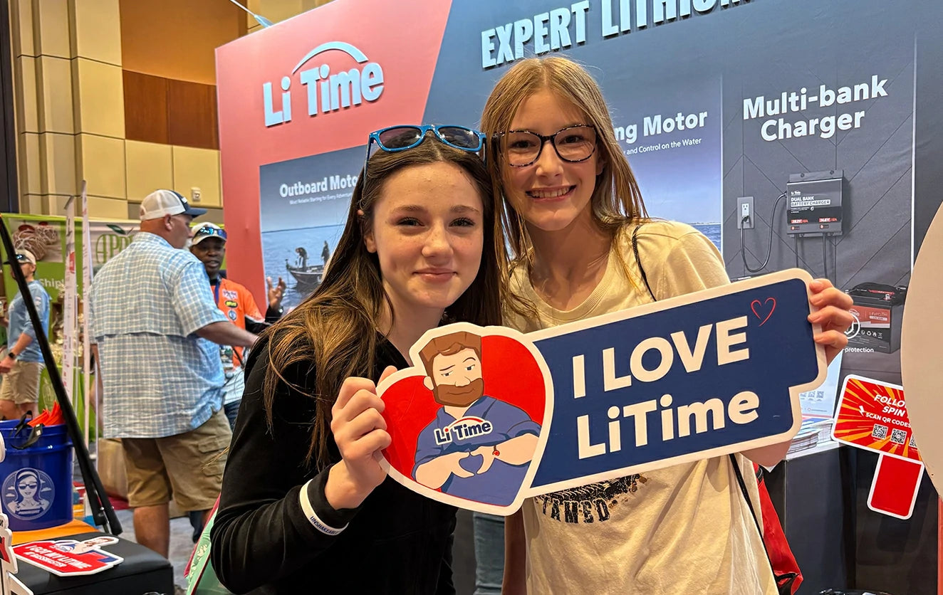 young fans at LiTime's Bass Master booth, holding 'I LOVE LiTime' and heart-shaped brand mascot signs